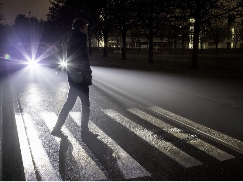 Ein Fußgänger geht nachts über einen Fußgängerüberweg im Scheinwerferlicht eines Autos.
